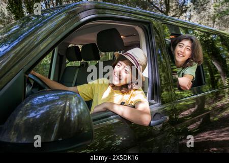 Deux jeunes garçons roulent dans un van, l'un d'eux porte un T-shirt jaune. Ils sourient et regardent par la fenêtre. L'un d'eux prétend conduire whil Banque D'Images