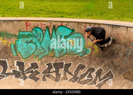 Jeune en chemise noire et casque vert accroupis sur son scooter cascadeur au Wilderness Skate Park, Porthcawl UK. 27 avril 2024 Banque D'Images