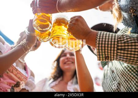 Groupe d'amis grillant joyeusement avec des tasses à bière sous un ciel lumineux à Oktoberfest ou Dult en allemagne Banque D'Images
