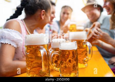 Mugs à bière sur une table dans une tente à bière avec des amis animés appréciant des bières et de la nourriture à oktoberfest ou dult Banque D'Images