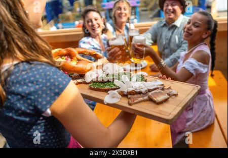 Serveuse servant un plateau en bois de nourriture allemande traditionnelle à un groupe de personnes joyeuses dans une tente de bière au festival oktoberfest ou dult en allemagne Banque D'Images