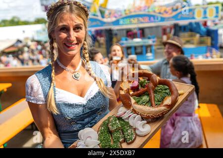 Serveuse souriante en robe bavaroise traditionnelle ou dirndl tenant un plateau en bois avec de la nourriture allemande traditionnelle dans une tente à bière au festival oktoberfest Banque D'Images