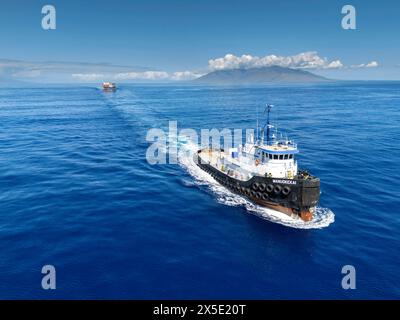 Une vue aérienne du remorqueur Manuokekai tirant une barge avec des conteneurs maritimes à travers le canal Alalakeiki, South Maui, Hawaii, États-Unis. Banque D'Images