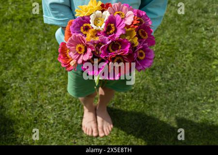 bouquet de fleurs lumineuses dans les mains d'un enfant pieds nus debout sur la pelouse par une journée d'été ensoleillée. Cadeau de fleur pour maman ou grand-mère. joie, joyeuse p Banque D'Images