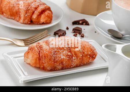 quelques xuixos de crema, pâtisseries typiques de catalogne, espagne, remplies de crème anglaise, sur différentes assiettes en céramique blanche, sur une table à côté d'une tasse de café Banque D'Images