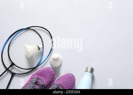 Volants de badminton en plume, raquettes, baskets et bouteille sur fond gris, pose à plat. Espace pour le texte Banque D'Images