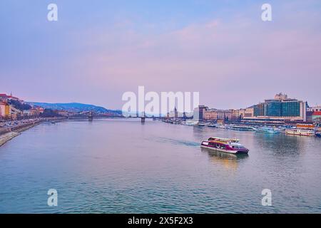 Le paysage urbain du soir avec les eaux violettes du Danube, le pont des chaînes Szechenyi et le ferry touristique, flottant le long de la vieille ville de Budapest, Hongrie Banque D'Images