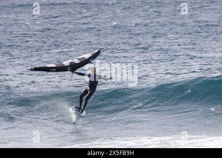 Agaete, Espagne - 21 janvier 2024 : personne faisant du Wing surf avec une grande vague se brisant au premier plan. Planche stationnaire au-dessus de la surface de l'eau Banque D'Images