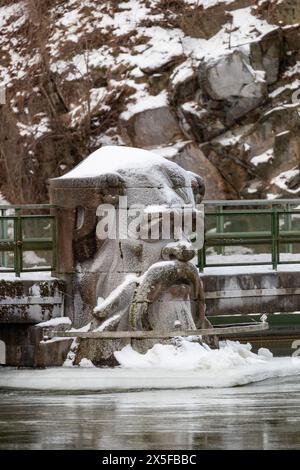 Trollhättan, Suède - 14 janvier 2024 : pylône en béton en forme de tête gelé avec de la glace et de la neige à la centrale électrique avec l'eau courante de la rivière. Aucune personne visible Banque D'Images