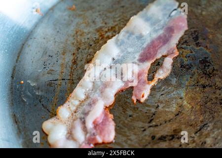 Un morceau de bacon est frit dans une casserole gros plan. Photo de haute qualité Banque D'Images