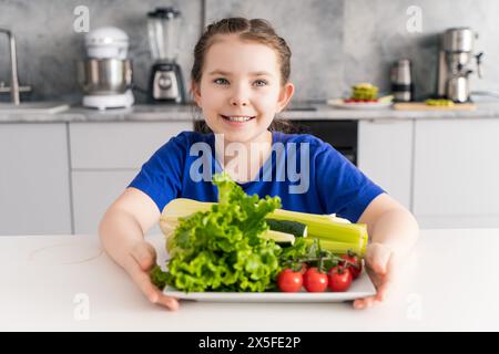 Portrait d'une petite fille heureuse avec une assiette de légumes. Adolescente dans la cuisine à la maison sur une assiette de légumes assortis. Photo de haute qualité Banque D'Images