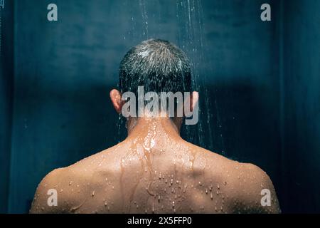 Homme prenant une douche se relaxant sous l'eau tombant de la pomme de douche de pluie. Guy douchant soins corporels. Banque D'Images