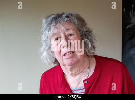 Une femme mature avec les cheveux gris debout et dans un cardigan rouge foncé et regardant principalement la caméra avec une expression sérieuse Banque D'Images