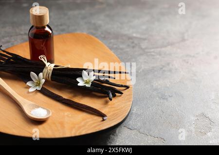 Bouquet de gousses de vanille, fleurs, sucre et bouteille d'huile essentielle sur table texturée grise, gros plan. Espace pour le texte Banque D'Images