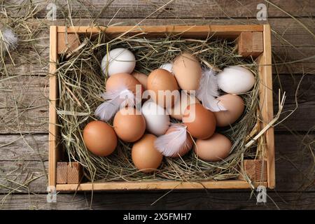 Oeufs de poule frais et foin séché dans une caisse sur une table en bois, vue de dessus Banque D'Images