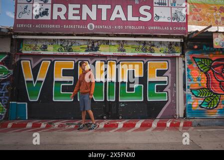 Personne marchant devant le magasin de location Venice Beach avec une vitrine de style graffiti. Banque D'Images