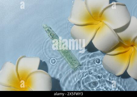 Ampoule de soin de la peau et belles fleurs de plumeria dans l'eau sur fond bleu clair, pose plate Banque D'Images