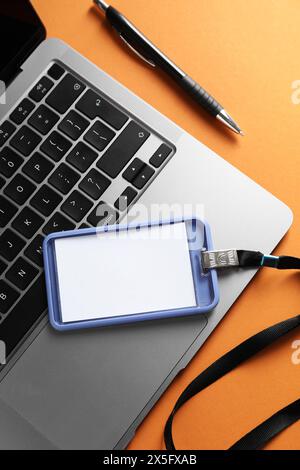 Badge vierge, stylo et ordinateur portable sur fond orange, vue de dessus Banque D'Images