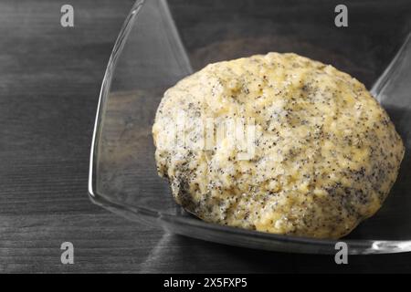 Pâte crue avec des graines de pavot dans un bol sur une table en bois noir, gros plan Banque D'Images