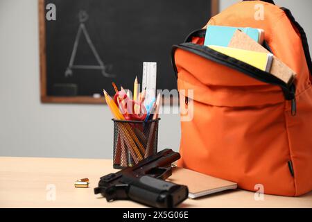 Arme à feu, balles et papeterie scolaire sur une table en bois près du tableau noir à l'intérieur, espace pour le texte Banque D'Images