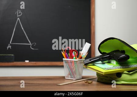 Arme à feu, balles et papeterie scolaire sur une table en bois près du tableau noir à l'intérieur, espace pour le texte Banque D'Images