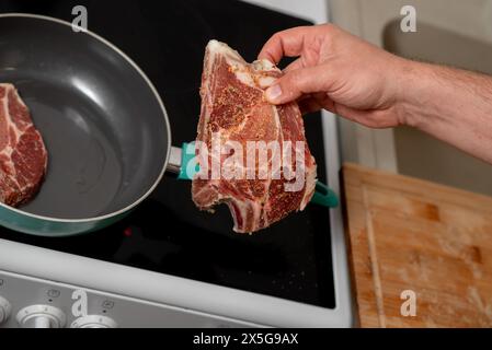 Une personne tient un morceau de viande sur un poêle. La viande est cuite et assaisonnée Banque D'Images