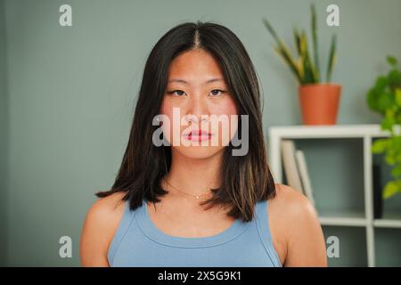 Gros plan portrait individuel d'une jeune femme asiatique sérieuse regardant la caméra debout à la maison Linving Room. Une femme chinoise penghtufl avec l'expression confiante, pensive et sombre vraie fille froncant les sourcils. Photo de haute qualité Banque D'Images