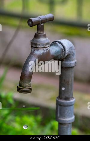 Un robinet rouillé coule de l'eau. L'eau tombe du robinet et sur le sol Banque D'Images