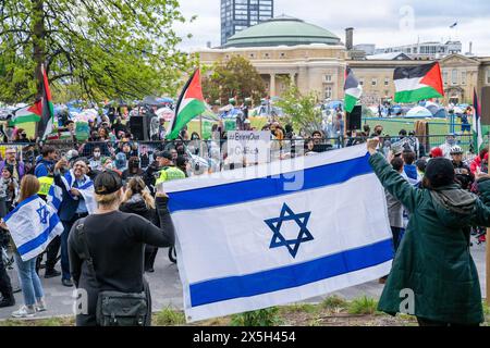 Les manifestants brandissent un drapeau israélien tandis que les manifestants pro-palestiniens lèvent des drapeaux palestiniens derrière eux pendant la manifestation. Manifestants pro-palestiniens et pro-israéliens à l'Université de Toronto devant le camp étudiant occupant King College Circle. Plaidant pour les droits des Palestiniens, les étudiants et les professeurs ont affiché des banderoles illustrant le sort des Palestiniens, des messages anti-sionistes et anti-israéliens, tandis que les manifestations pro-israéliennes ont impliqué des étudiants et des sympathisants en agitant des drapeaux israéliens et en engageant des dialogues pour défendre les actions et les politiques d'Israël. Banque D'Images