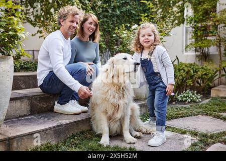 Parents, chien et enfant dans le portrait de cour avec sourire, liaison et plaisir ludique avec animal de compagnie le week-end d'été. Maman, papa et fille enfant ensemble avec Banque D'Images