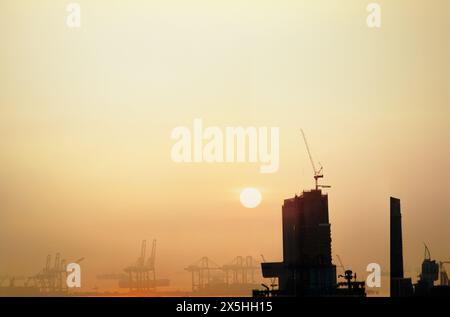 à propos de la grue à tour installée sur le bâtiment et derrière se trouvent le port et la logistique parmi le coucher du soleil Banque D'Images