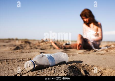 Une scène stimulante montrant une femme se lamentant sur la pollution alors qu'elle est assise près d'une bouteille en plastique jetée sur une plage de sable, symbolisant les devas Banque D'Images