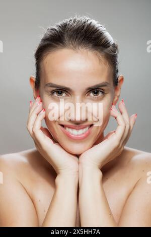 Cette image capture le sourire radieux et les yeux étincelants d'une jeune femme, encadrés par ses mains avec des ongles rouges manucurés. Banque D'Images