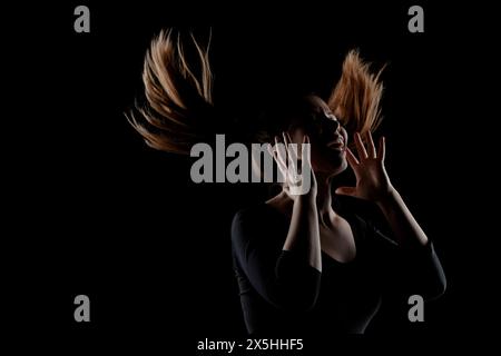 Une image frappante d'une femme capturée avec ses cheveux jetés dramatiquement dans l'air, silhouettée sur un fond noir pur, soulignant le mouvement A. Banque D'Images