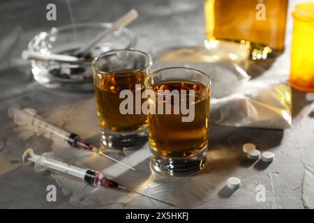 Alcoolisme et toxicomanie. Whisky dans des verres, seringues, pilules et cocaïne sur table grise Banque D'Images