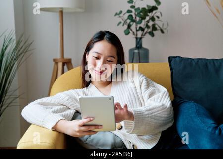 Une femme assise sur un canapé est concentrée sur une tablette Banque D'Images