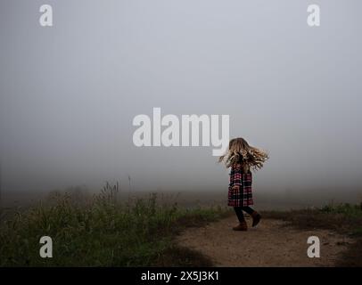 Petite fille en manteau à carreaux explorant un champ brumeux Banque D'Images