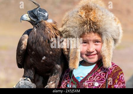 Asie, Mongolie, Province de Bayan-Oglii. Altaï Eagle Festival, portrait d'un jeune garçon kazakh dans son chapeau de fourrure traditionnel avec son aigle. (Usage éditorial uniquement) Banque D'Images