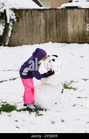 Enfant en équipement d'hiver façonne adorablement un bonhomme de neige. Banque D'Images
