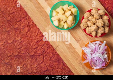 Divers plats de légumes prêts à cuire sur une planche à découper en bois. Trois bols de machine à repas et tranches de pommes de terre et d'oignons. Banque D'Images