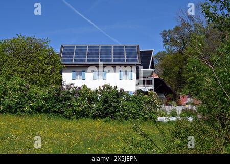 Panneaux solaires ou photovoltaïques installés sur le toit d’une maison familiale blanche observée pendant une journée ensoleillée dans un village suisse. Banque D'Images