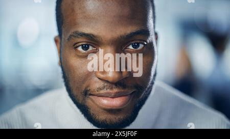 Gros plan Portrait d'un bel homme noir aux yeux brun profond, barbe taillée, à col roulé blanc élégant, clin d'œil et montre un sourire parfait. Attrayant Authentic Gentleman regarde la caméra Banque D'Images