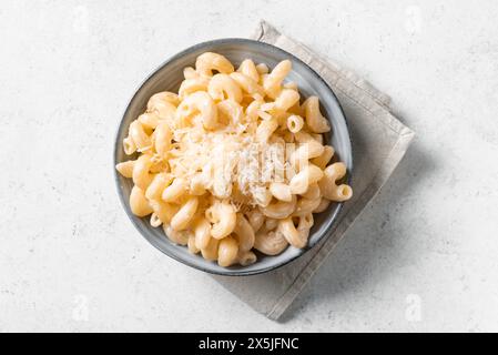 Mac et fromage sur fond de béton blanc, vue de dessus, espace de copie. Bol de pâtes crémeuses Alfredo Cavatappi avec parmesan râpé. Banque D'Images