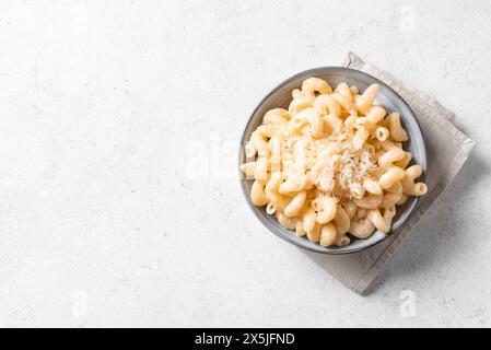 Mac et fromage sur fond de béton blanc, vue de dessus, espace de copie. Bol de pâtes crémeuses Alfredo Cavatappi avec parmesan râpé. Banque D'Images