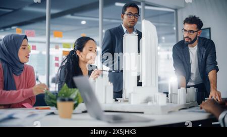 Réunion de bureau de l'agence d'architecture multiethnique moderne. Groupe d'architectes professionnels, concepteurs, développeurs, investisseurs utilisent modèle de bâtiment pour concevoir un projet de logement durable et éconergétique Banque D'Images