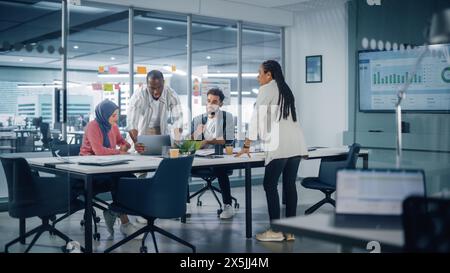 Réunion de la salle de conférence du bureau multiethnique : équipe multiculturelle de quatre entrepreneurs créatifs discutent, discutent de la stratégie de croissance. Divers jeunes gens d'affaires travaillent sur Digital e-commerce Startup. Banque D'Images
