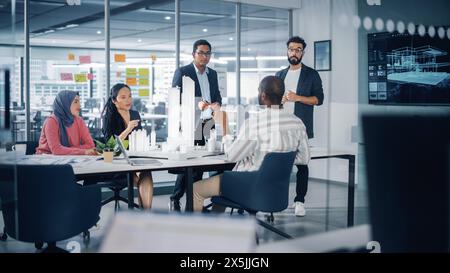 Réunion de bureau de l'agence d'architecture multiethnique moderne. Groupe d'architectes professionnels, concepteurs, développeurs, investisseurs utilisent la télévision avec modèle de bâtiment 3D pour concevoir un projet de logement durable Banque D'Images