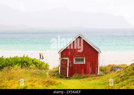 Deux personnes marchant sur la plage de Ramberg un jour d'automne, avec une cabane célèbre au premier plan, les îles Lofoten, Nordland, Norvège, Scandinavie, Europe Copyri Banque D'Images