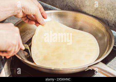 Une femme prépare de délicieuses crêpes dans une poêle de gros plan. Recette de crêpe suzette. Crêpe sur une poêle chromée. Foyer sélectionné. Photo de haute qualité Banque D'Images