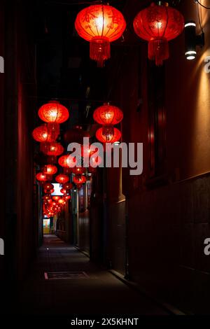 Ruelle sombre et étroite illuminée par des lanternes chinoises rouges suspendues au Chinatown de Bangkok, en Thaïlande, dans la soirée. Banque D'Images